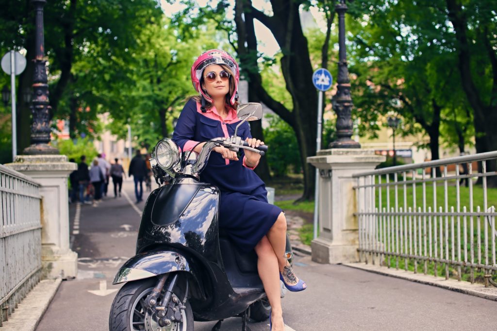 A woman in a dress sits on a moto scooter.