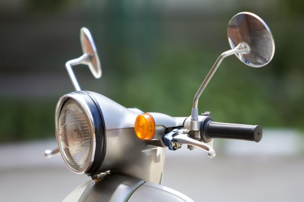Close-up detail of new white shiny motorbike with round headlight, two mirrors and manual brake